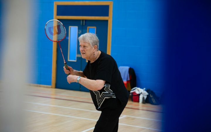 Adult beginners learning badminton together in a gymnasium